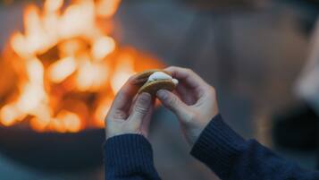 Una persona sostiene una galleta con un malvavisco frente a un fuego desenfocado.