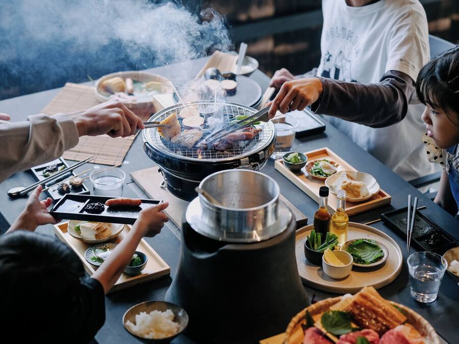 Un grupo de personas alrededor de una mesa con una parrilla, varios platos y una olla caliente.