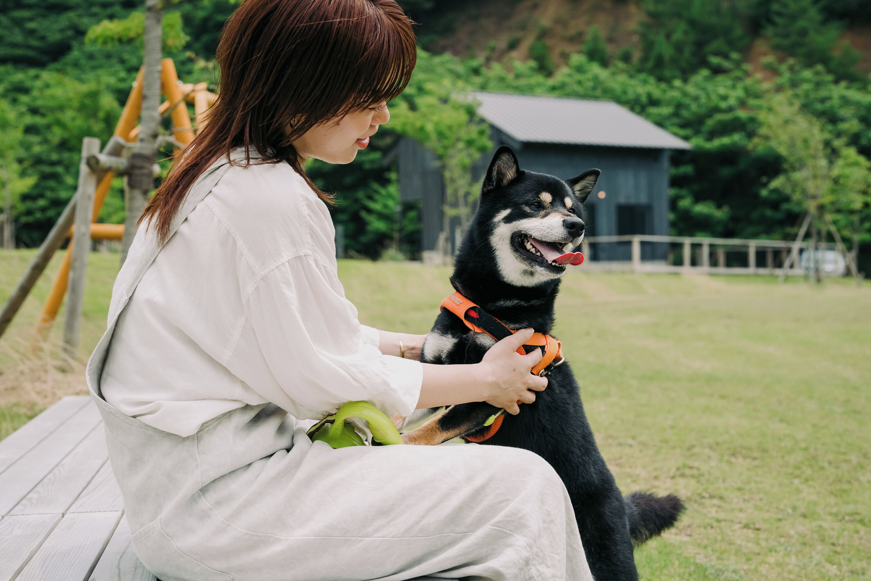 A person sitting on a bench outdoors, holding a dog on a leash.