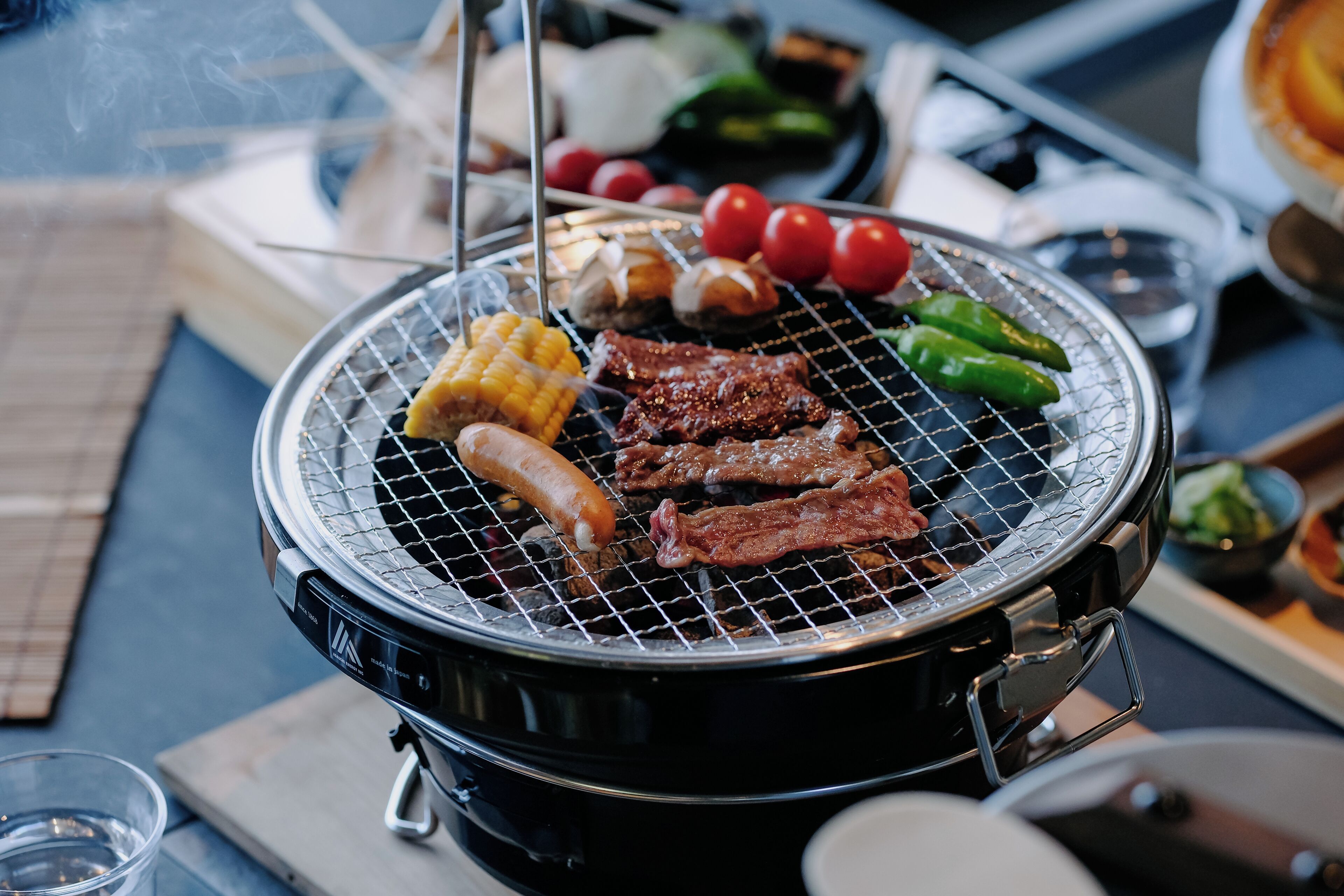 A portable grill with various meats and vegetables being cooked.