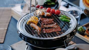 A portable grill with various meats and vegetables being cooked.
