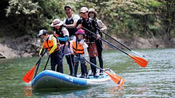 A group of people on a blue and white inflatable raft with orange paddles, standing on a calm body of water surrounded by trees.