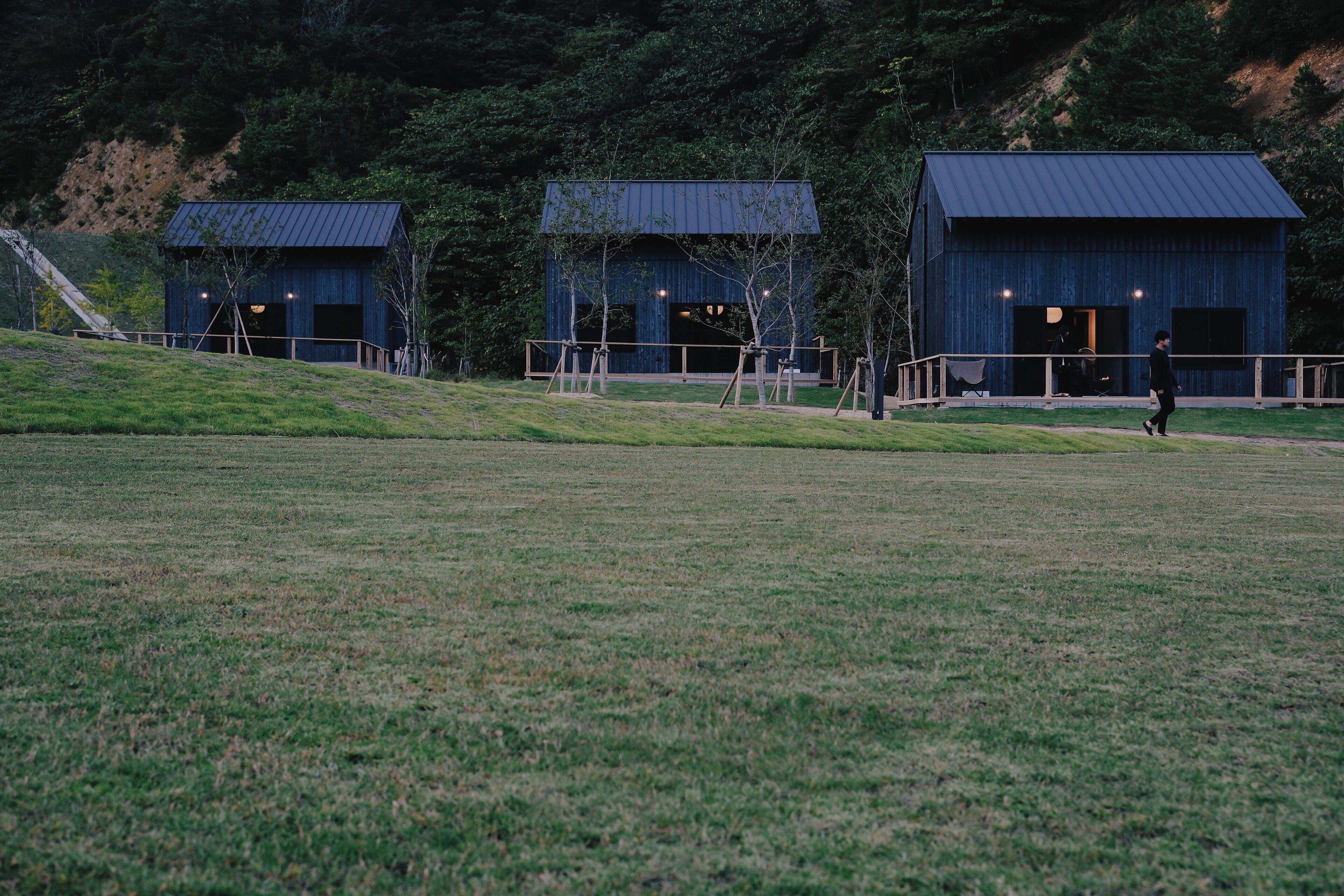 A building with a metal roof and large windows, surrounded by a grassy area and trees.