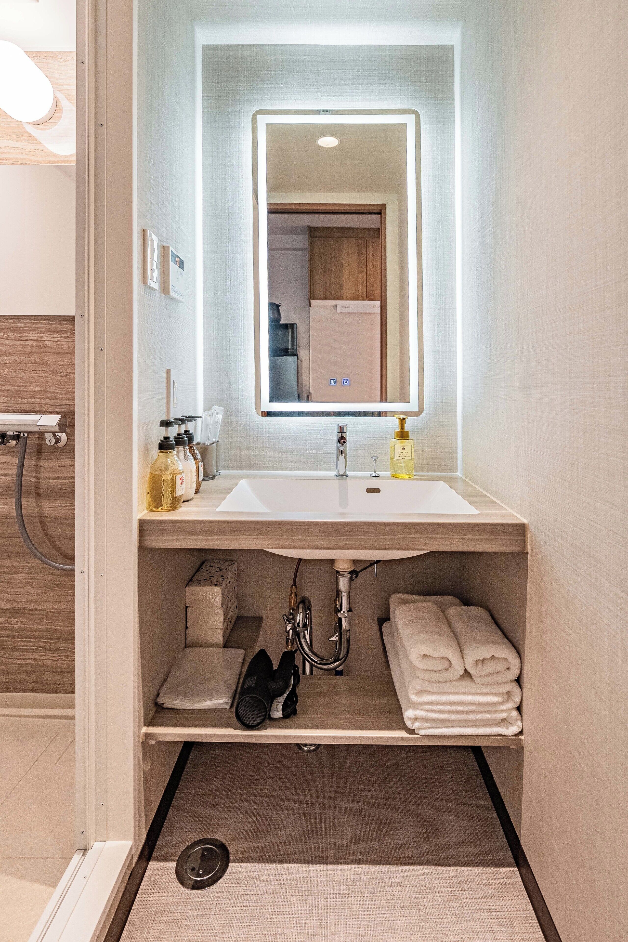 Casa de banho moderna com lavatório branco, espelho e espaço para toalhas.