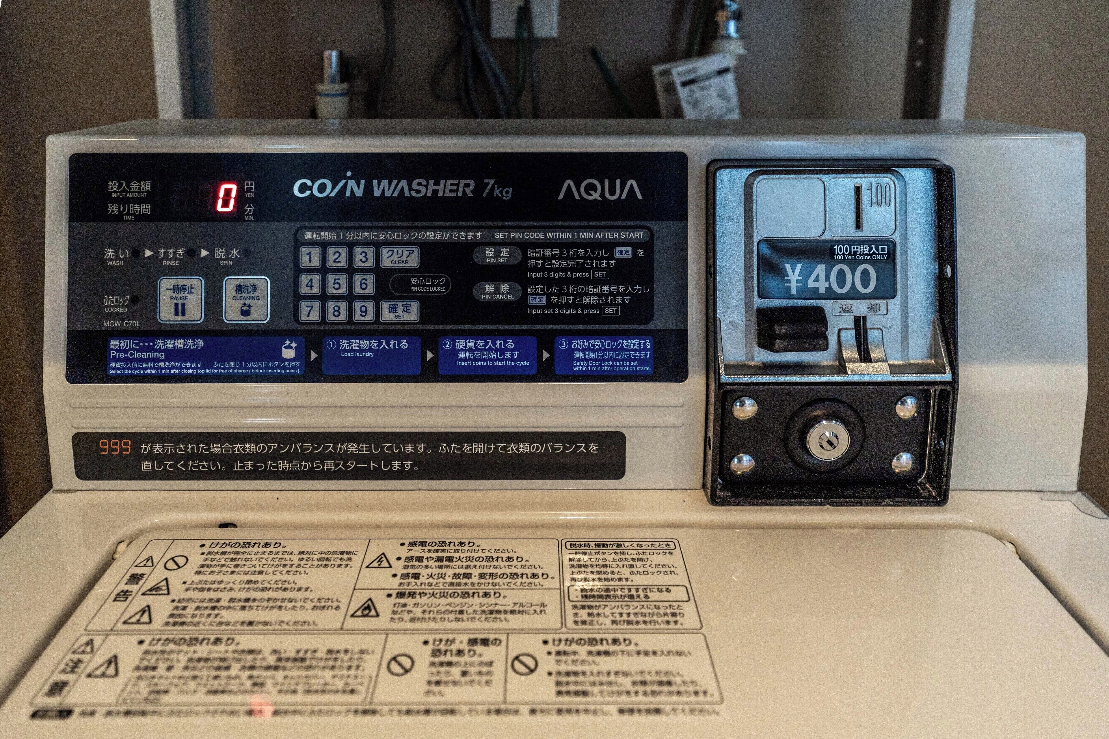 Una lavadora COIN WASHER de 7kg, con ranura para monedas de ¥400 e instrucciones en japonés.