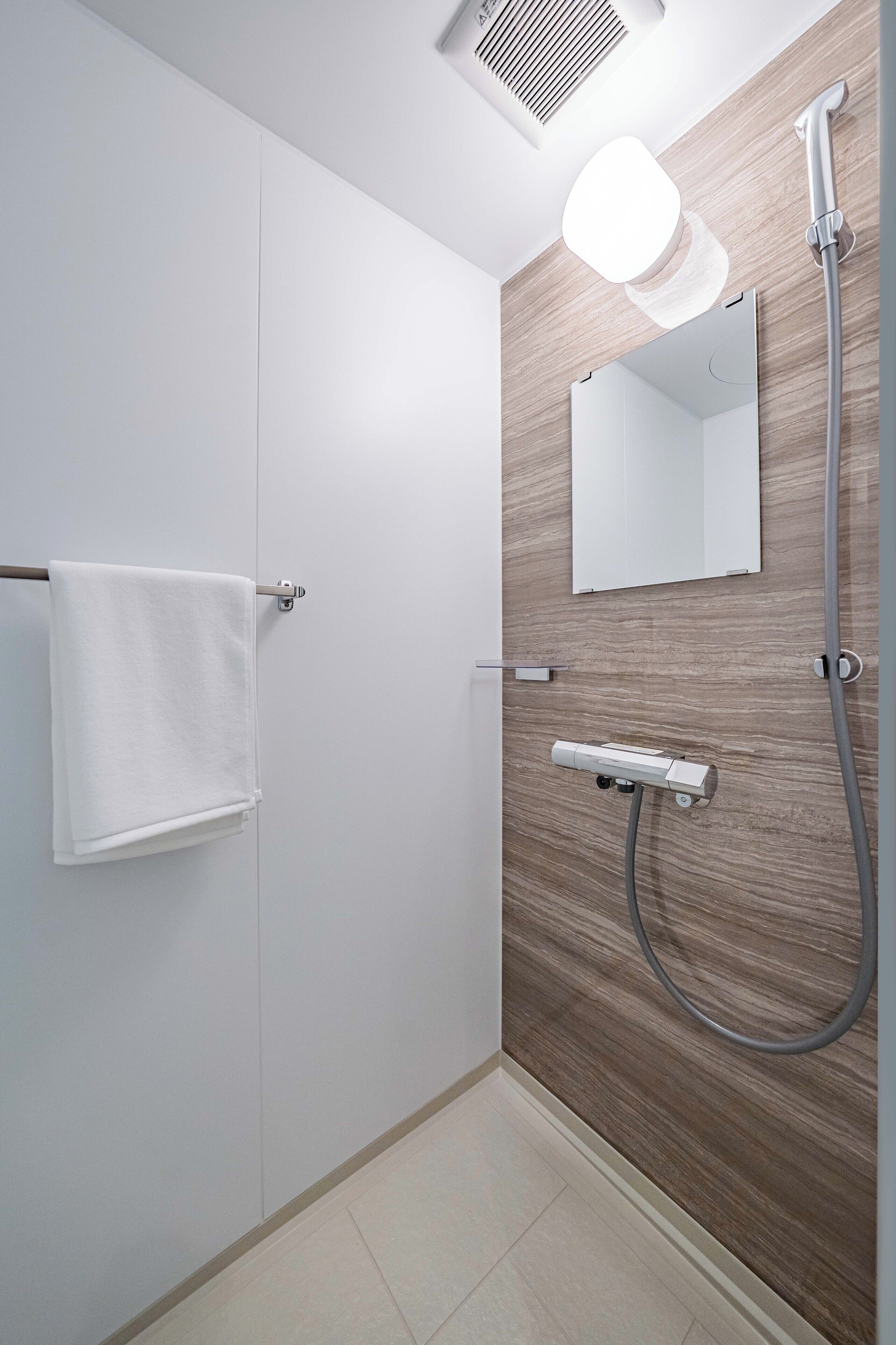 A modern bathroom with a wooden wall, a white towel rack, a mirror, and a shower with a handheld showerhead.