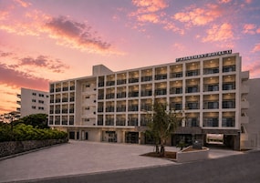 A multi-story hotel with a flat facade, multiple balconies, and a clear sky with clouds.