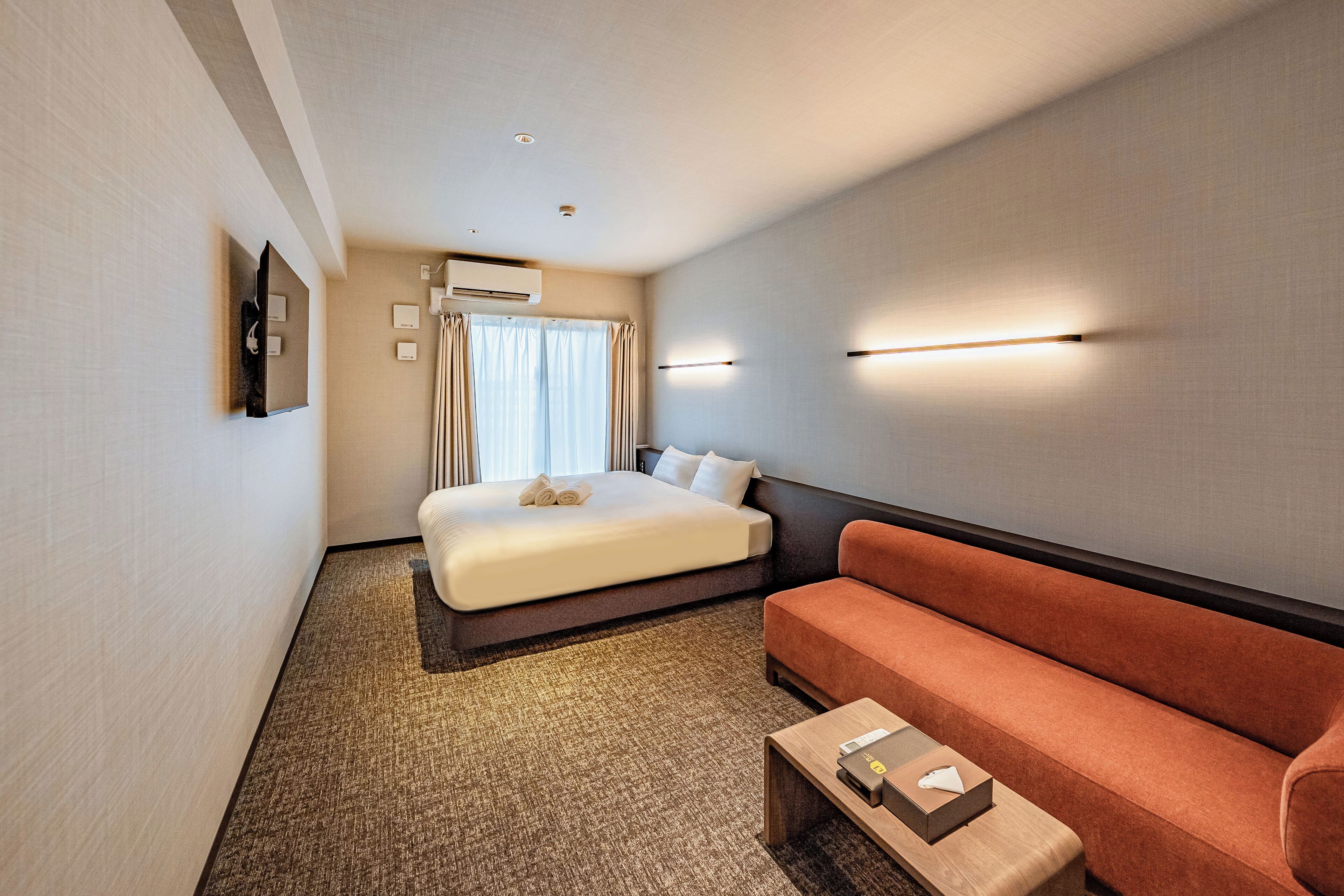 A hotel room with a bed, a sofa, a coffee table, and a wall-mounted TV.