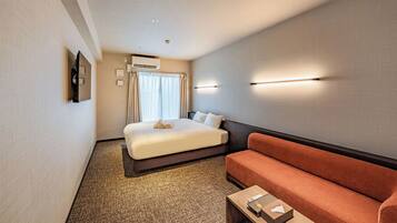 A hotel room with a bed, a sofa, a coffee table, and a wall-mounted TV.