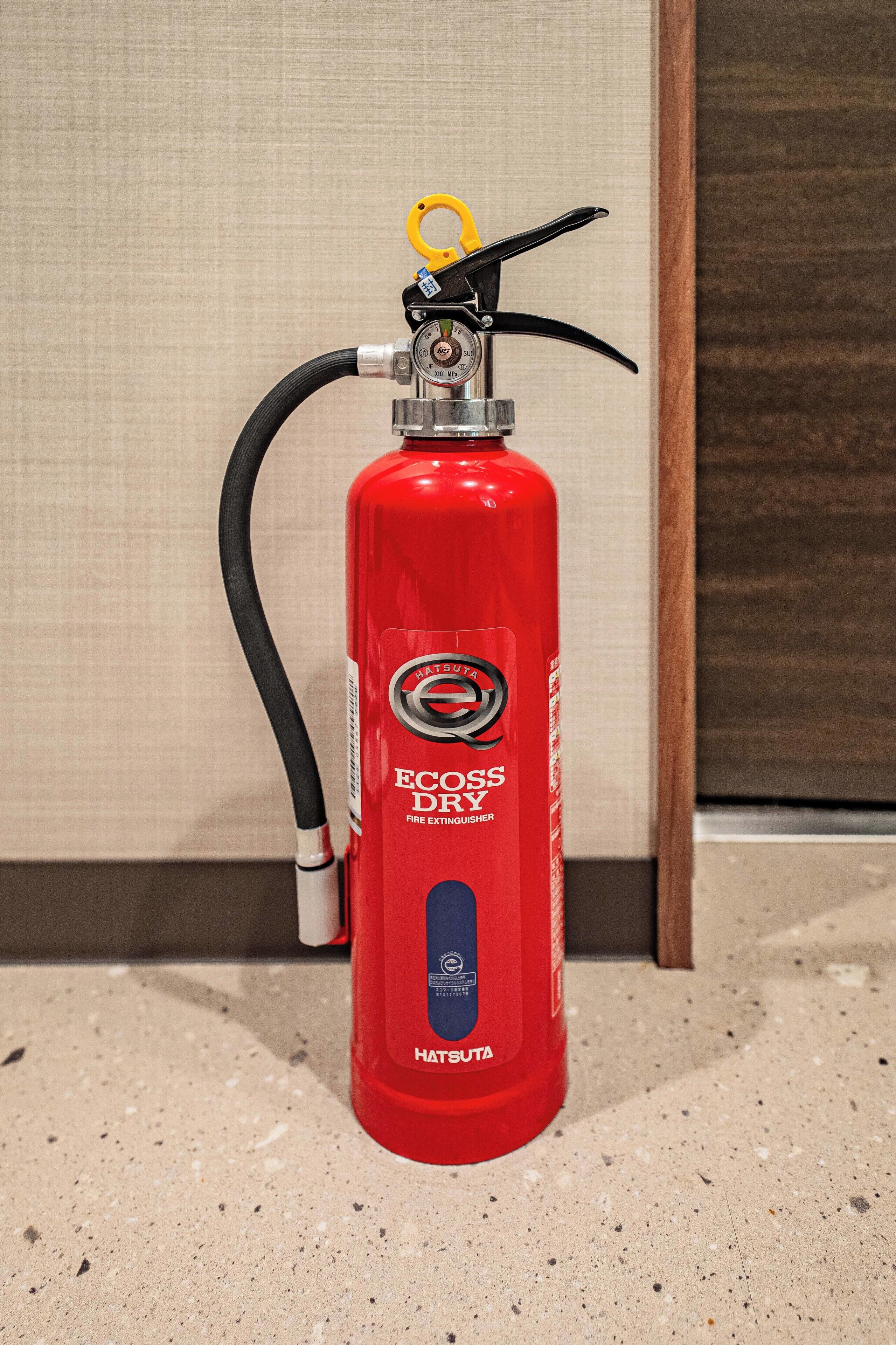A red fire extinguisher labeled "Hatsuta" on a speckled floor.
