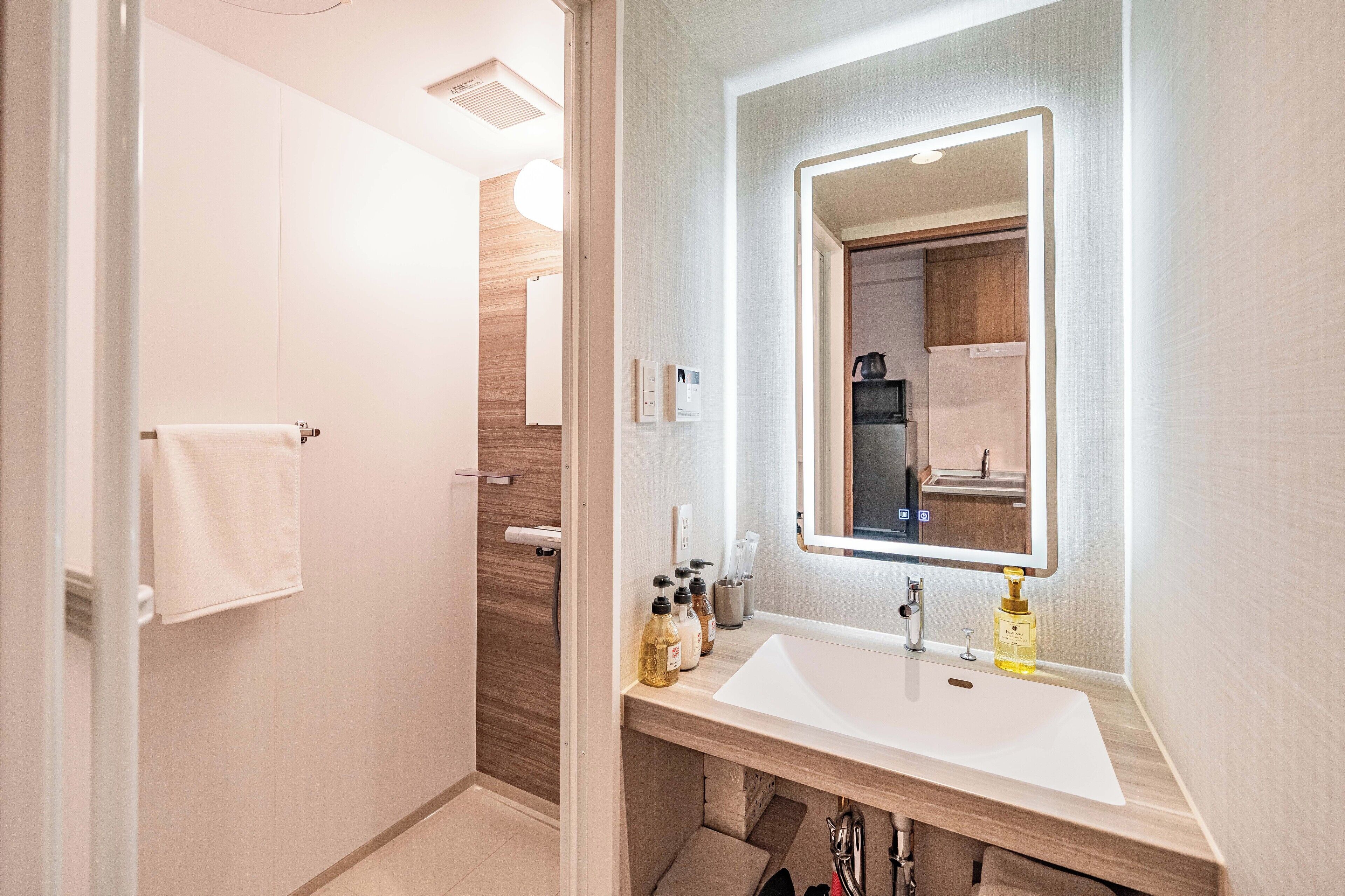 Une salle de bain moderne avec un lavabo blanc, un miroir doté d’un éclairage intégré et un espace douche.
