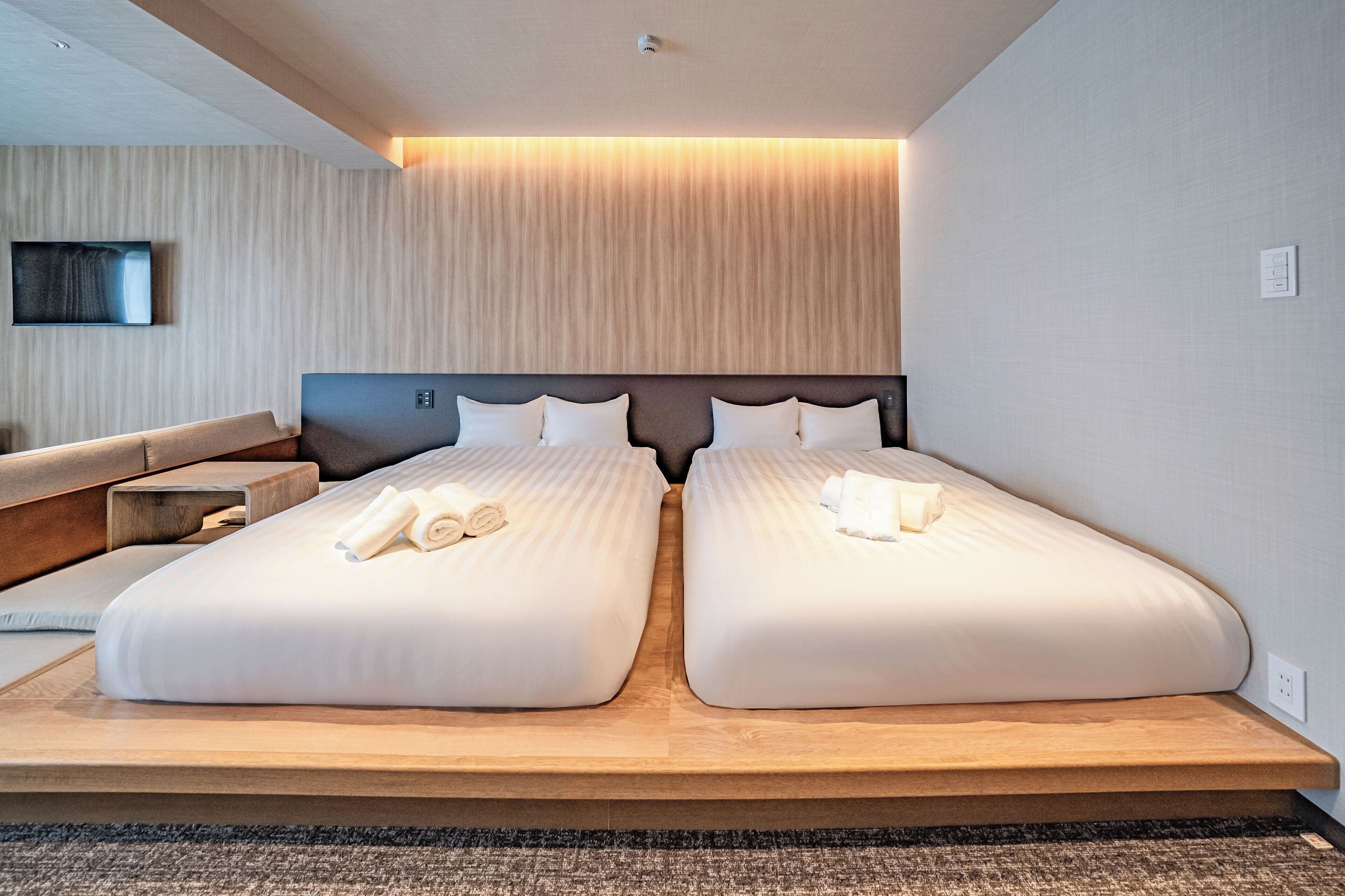 A hotel room with two beds, a wooden headboard, a flat-screen TV, and a wall-mounted light fixture.