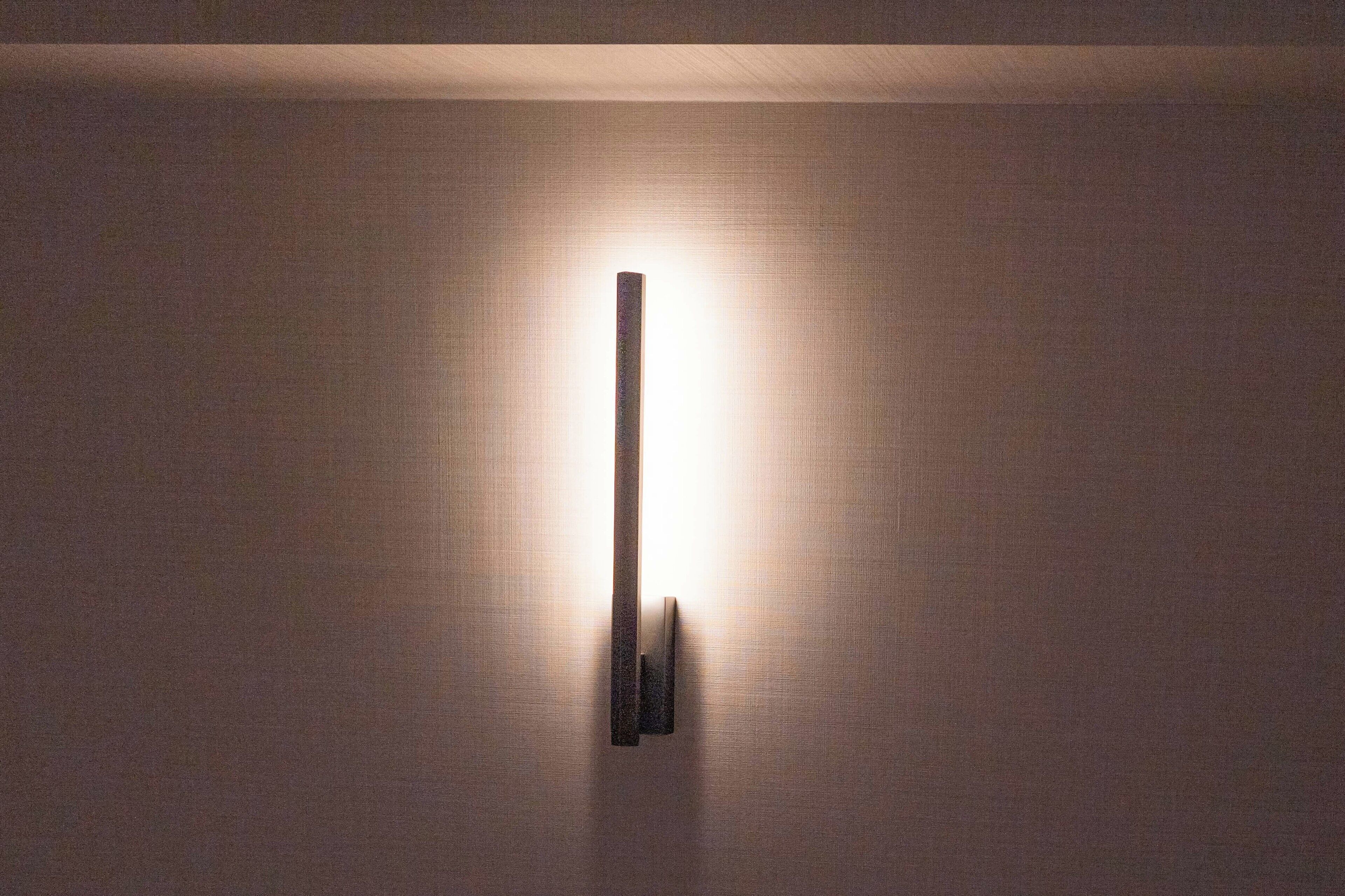 A wall-mounted light fixture with a vertical design and a single light source.