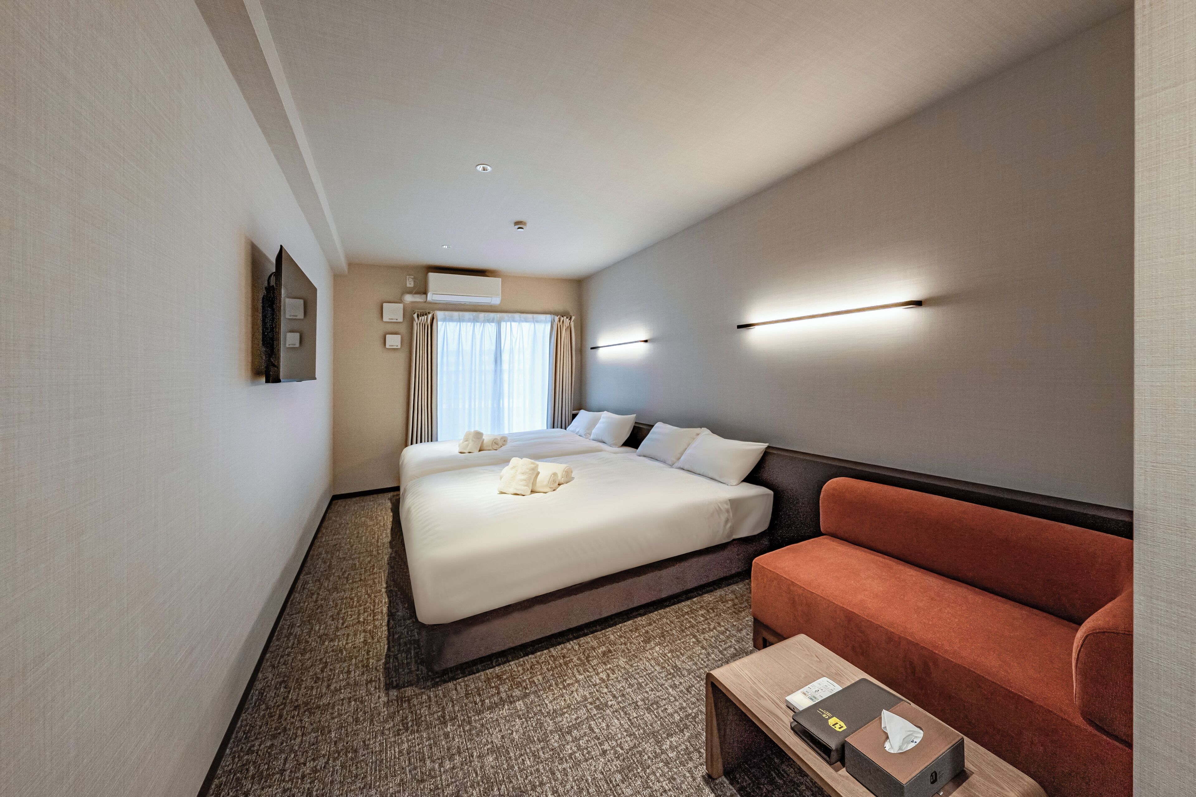 A hotel room with a large bed, a sofa, a small table, and a window with curtains.