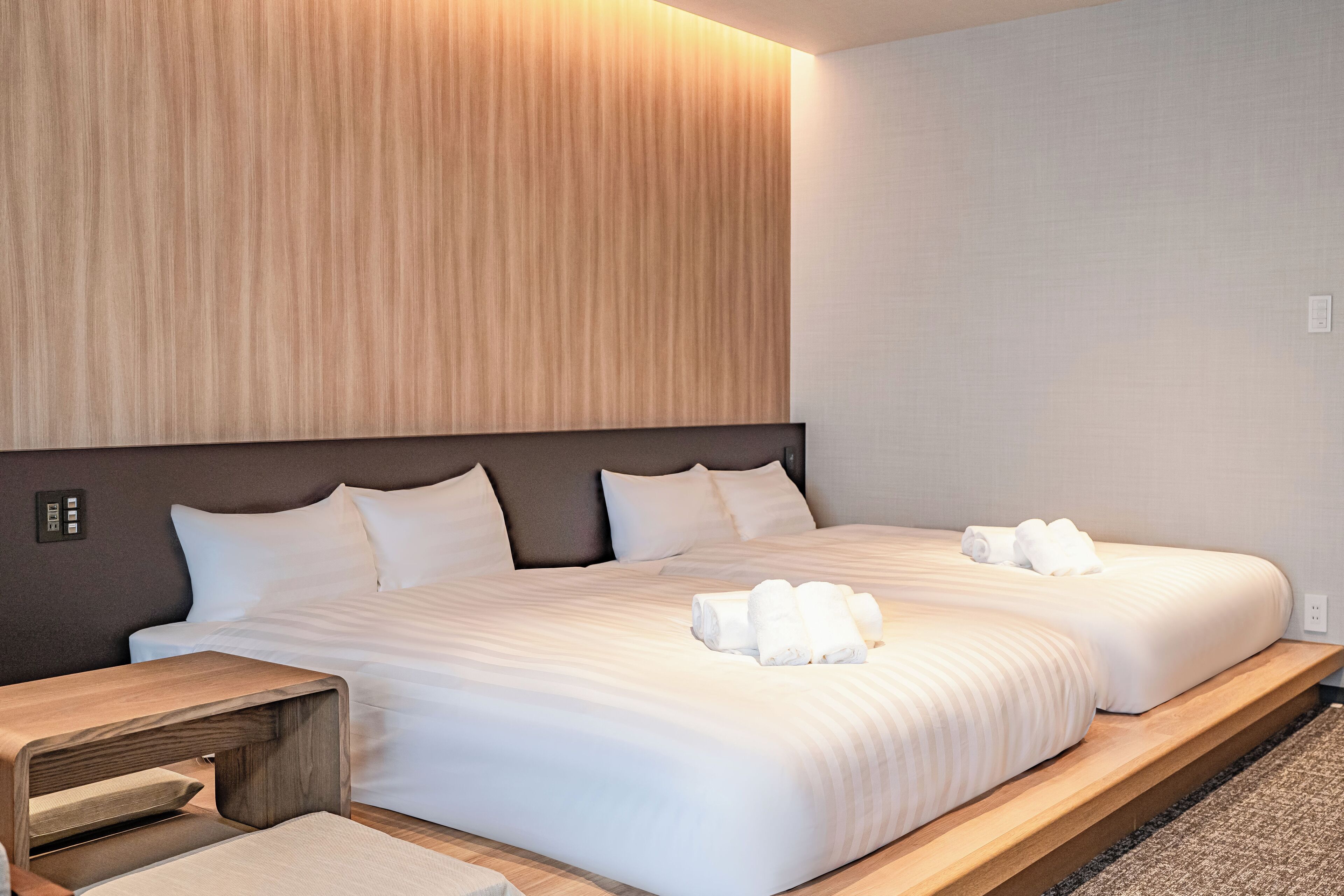 A modern hotel room with two beds, a wooden headboard, and a small wooden nightstand.