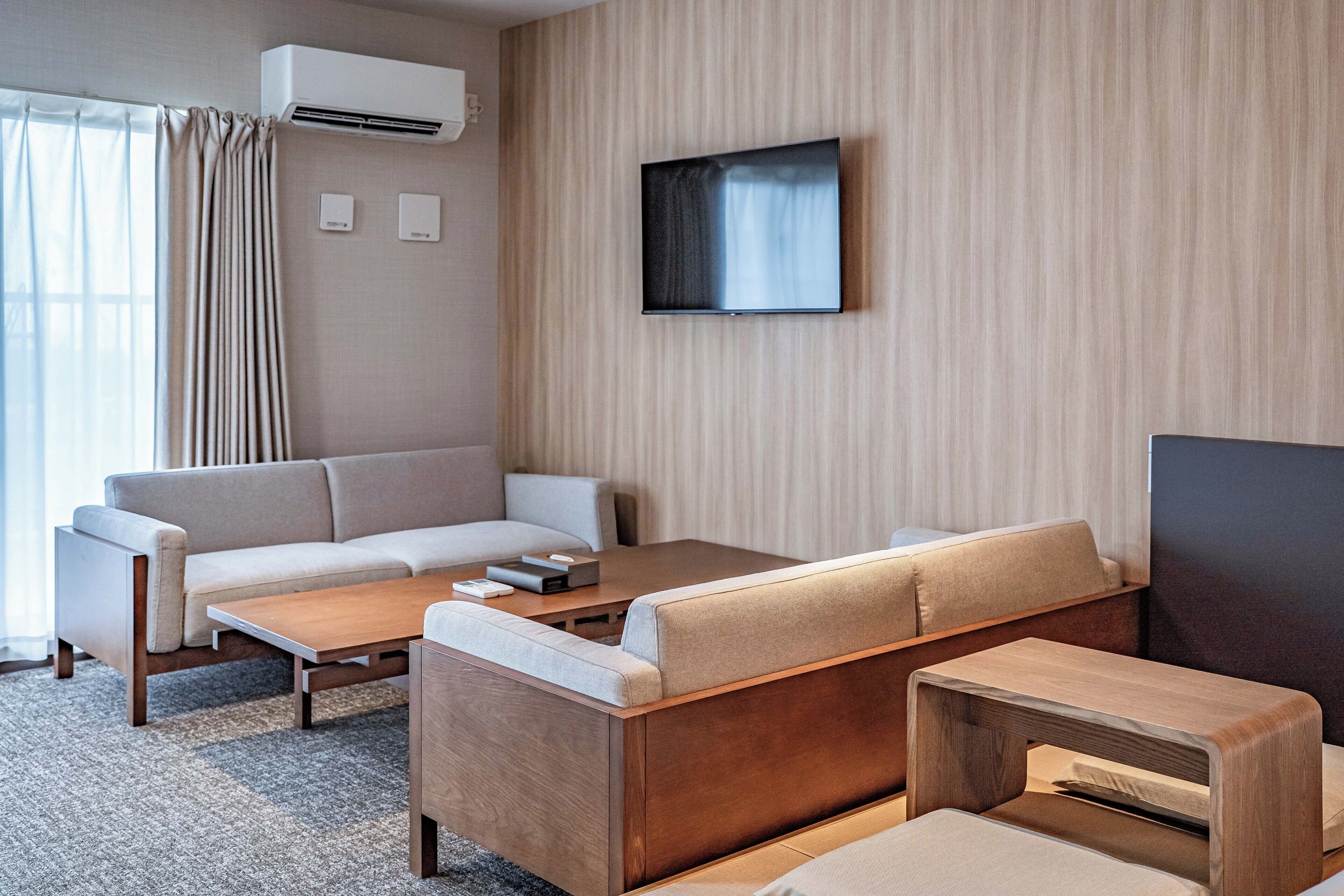 Una habitación de hotel moderna con sofá, una mesita de café y un televisor de pantalla plana montado en la pared.