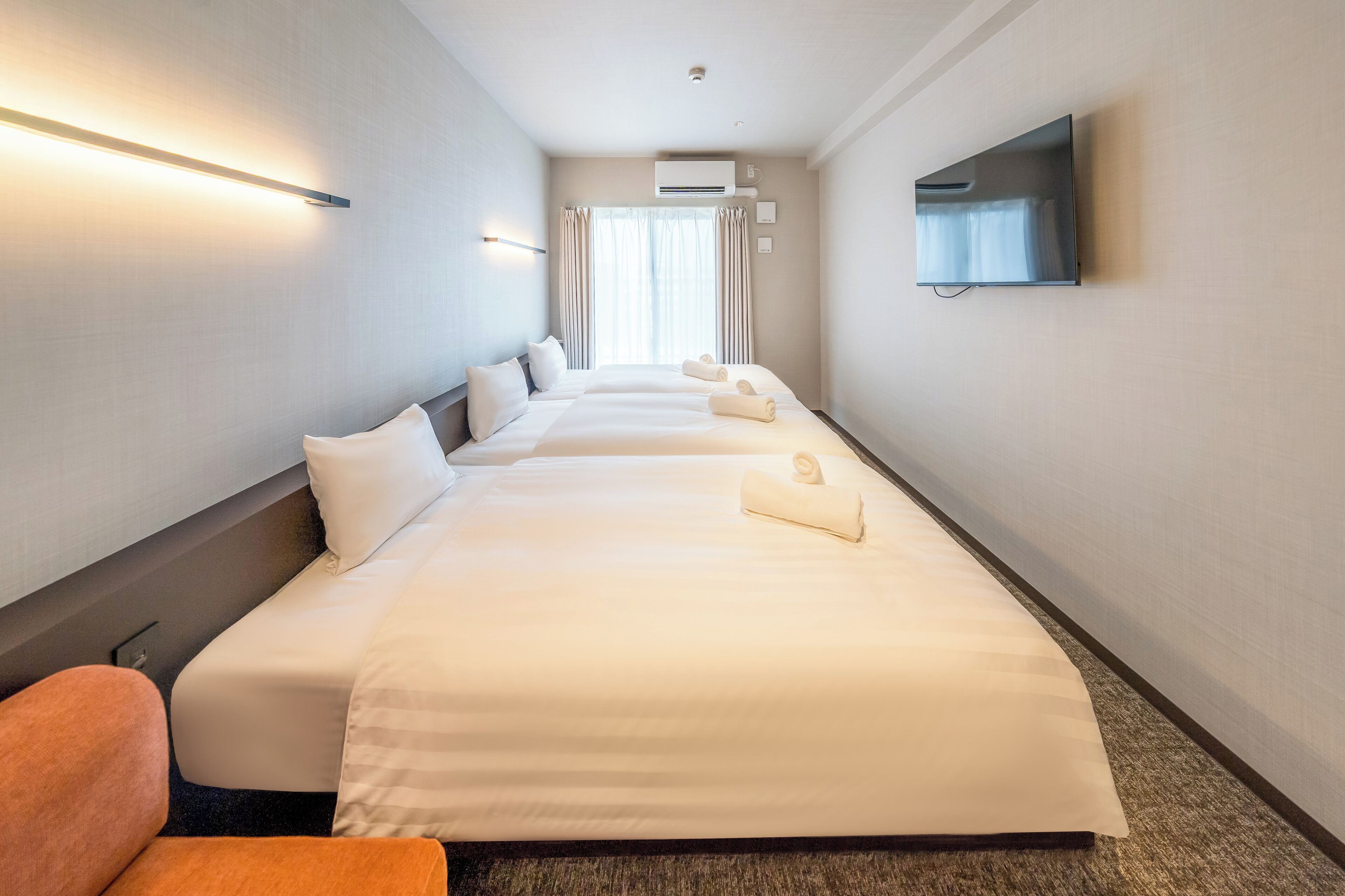 A hotel room with three beds, a flat-screen TV, and a large window with curtains.