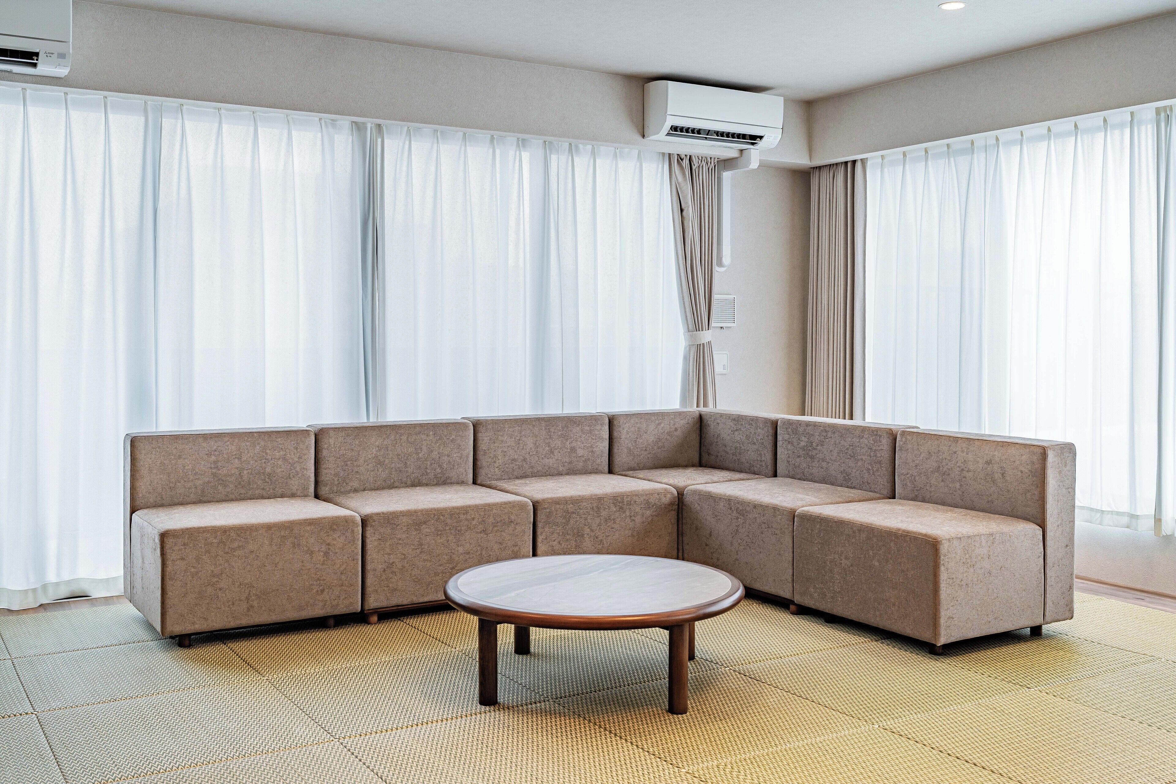 A modern living room with a sectional sofa, a round coffee table, and large windows with sheer curtains.