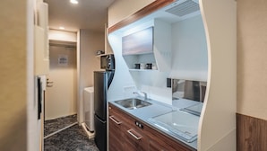 A compact kitchen with a built-in refrigerator, a sink, and wooden cabinetry. - Apartment Hotel 11 Nippombashi (Osaka)