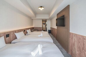 Ein Hotelzimmer mit drei Betten, einem an der Wand befestigten Flachbildfernseher und einer Deckenleuchte.