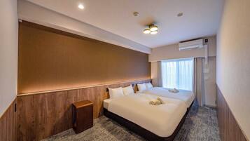 A hotel room with a large bed, a wooden headboard, a small wooden side table, and a ceiling-mounted air conditioning unit.