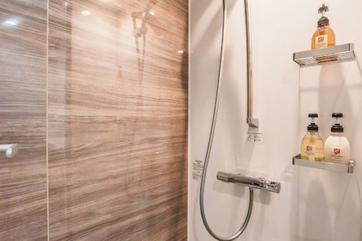 Ein modernes Badezimmer mit Marmorwand, einer Handbrause und zwei Ablagen für Toilettenartikel.