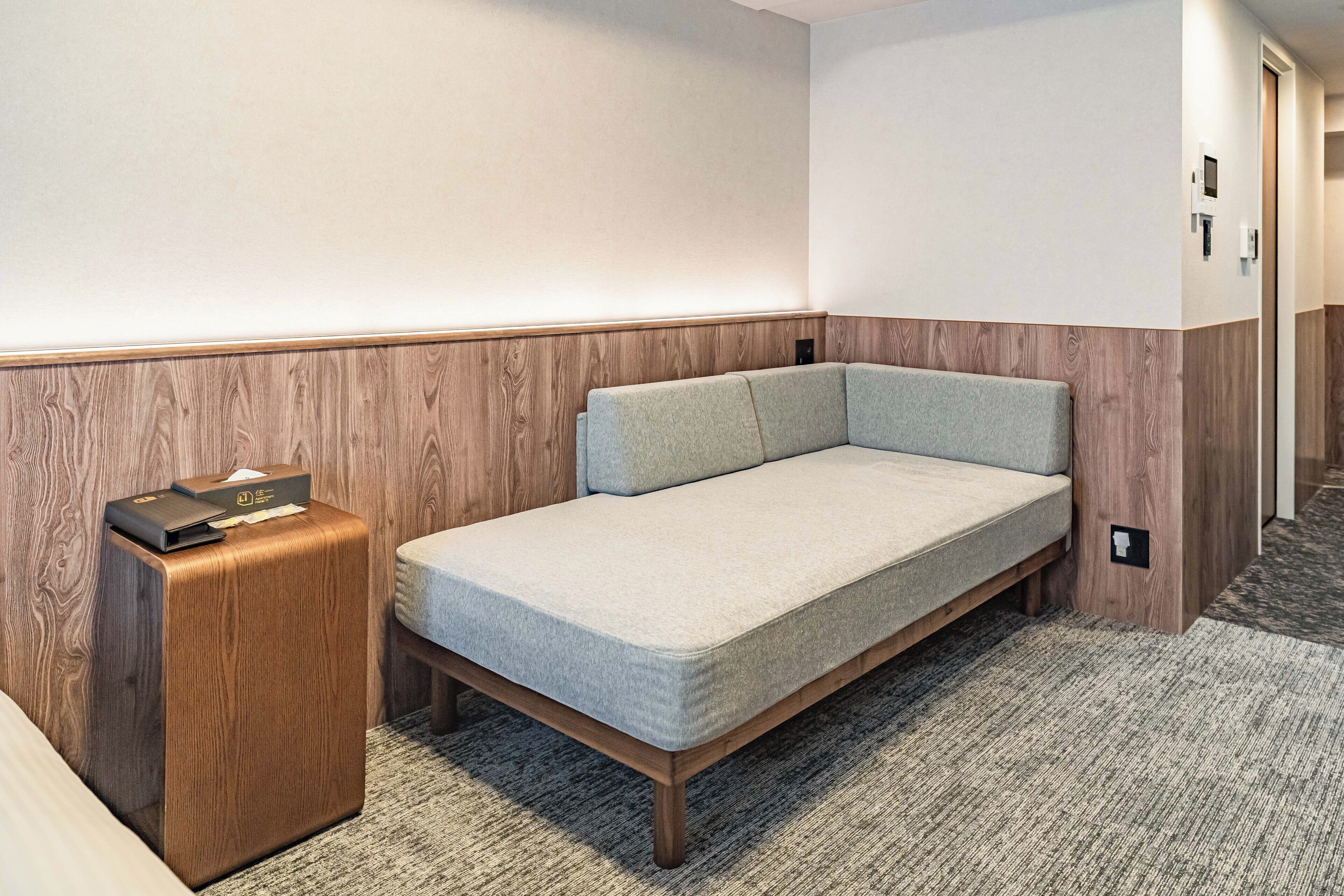 A compact room with a single bed, a small wooden nightstand, and a wall-mounted light fixture.