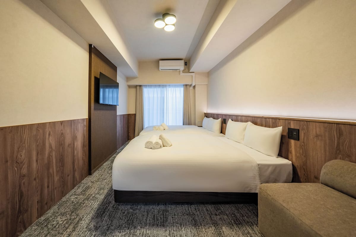 Une chambre d’hôtel dotée d’un grand lit, d’un téléviseur à écran plat fixé au mur, d’un système de climatisation et d’un sol recouvert de moquette.