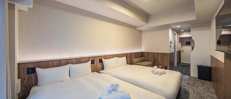 A hotel room with two beds, a wooden headboard, a carpeted floor, and a hallway leading to a bathroom.