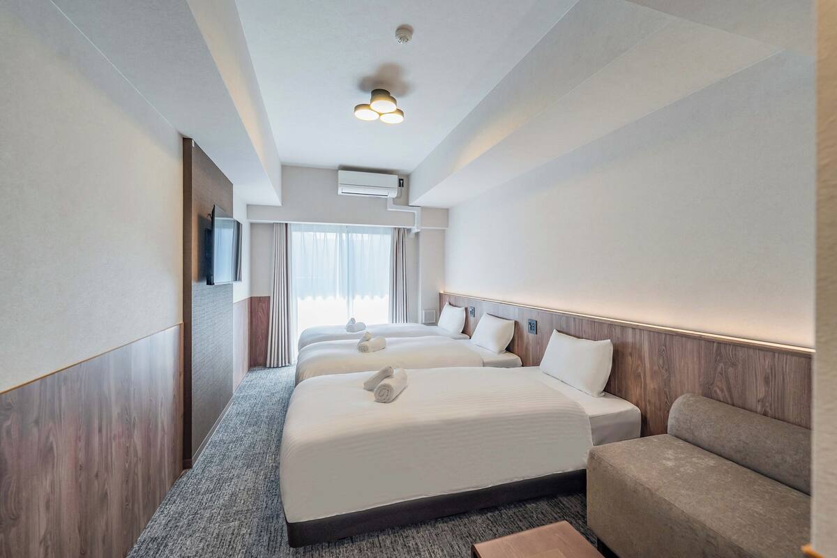 Une chambre d’hôtel avec trois lits, un canapé, un téléviseur à écran plat et un appareil de climatisation fixé au plafond.