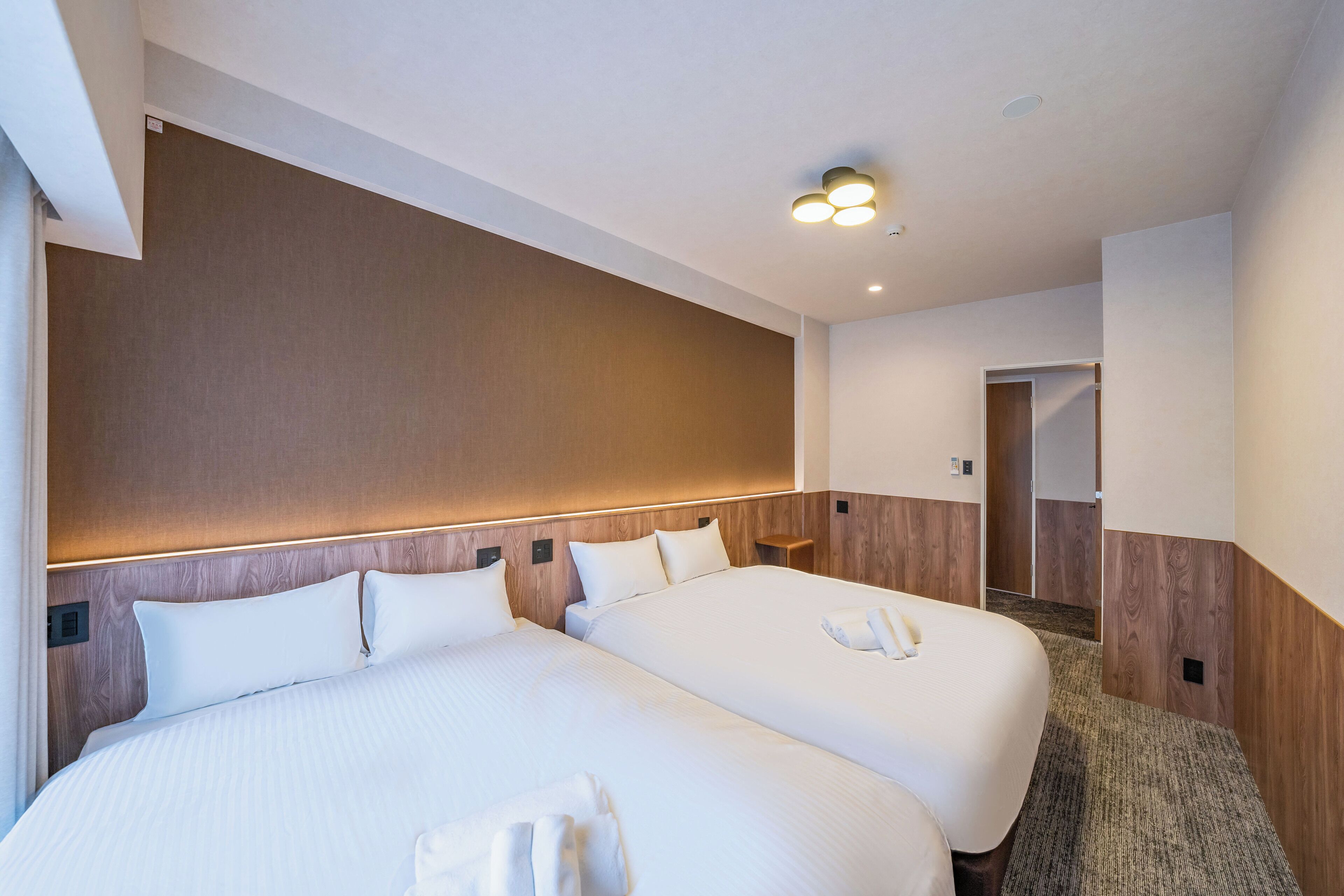 Ein Hotelzimmer mit zwei Betten, einem Holzkopfteil, Teppichboden und einer Deckenleuchte.