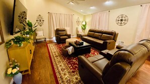 A living room with a brown leather sofa, a wooden cabinet with plants, a red patterned rug, and a ceiling fan. - Spacious 5-bedroom Wheelchair Accessible House in Pittsburgh (Pittsburgh)