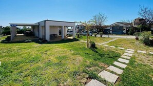 Une maison moderne dotée d’un patio couvert, d’une pelouse bien entretenue et d’un chemin en pierre menant à l’entrée.