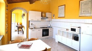 Une cuisine compacte avec des meubles blancs, une cuisinière et un four à micro-ondes. On y trouve une table à manger avec des chaises et un luminaire suspendu.