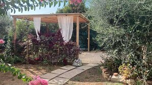 Un jardin agrémenté d’une pergola en bois recouverte d’un tissu blanc, entouré de différentes plantes et fleurs.