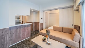 A modern living room with a sofa, a coffee table, and a small kitchen area with a counter and shelves. - Apartment Hotel 11 Higashi Umeda (Osaka)