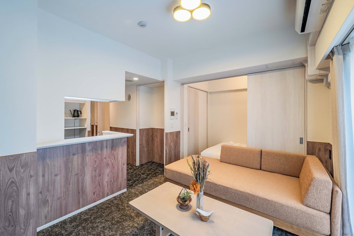 Een moderne woonkamer met een bank, een salontafel en een klein keukentje met een aanrecht en planken.