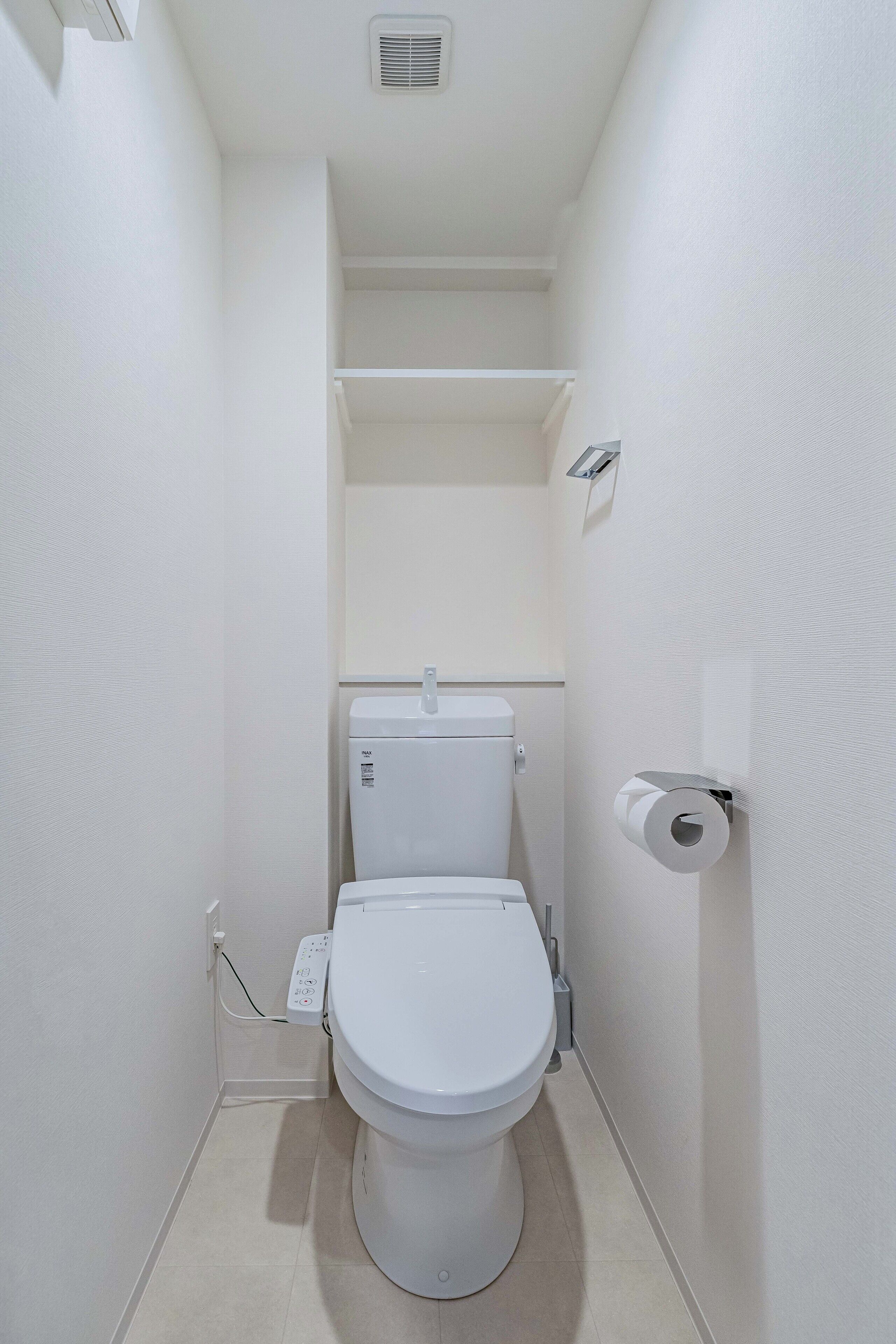 A compact, white bathroom with a toilet, a wall-mounted toilet paper holder, and a visible electrical outlet.