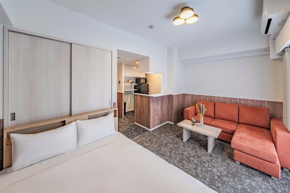 Una habitación de hotel con cama, sofá, una mesita y una zona de kitchenette.