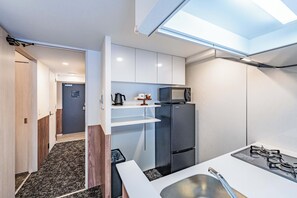 Una kitchenette compacta con microondas, refrigerador y estufa a gas.