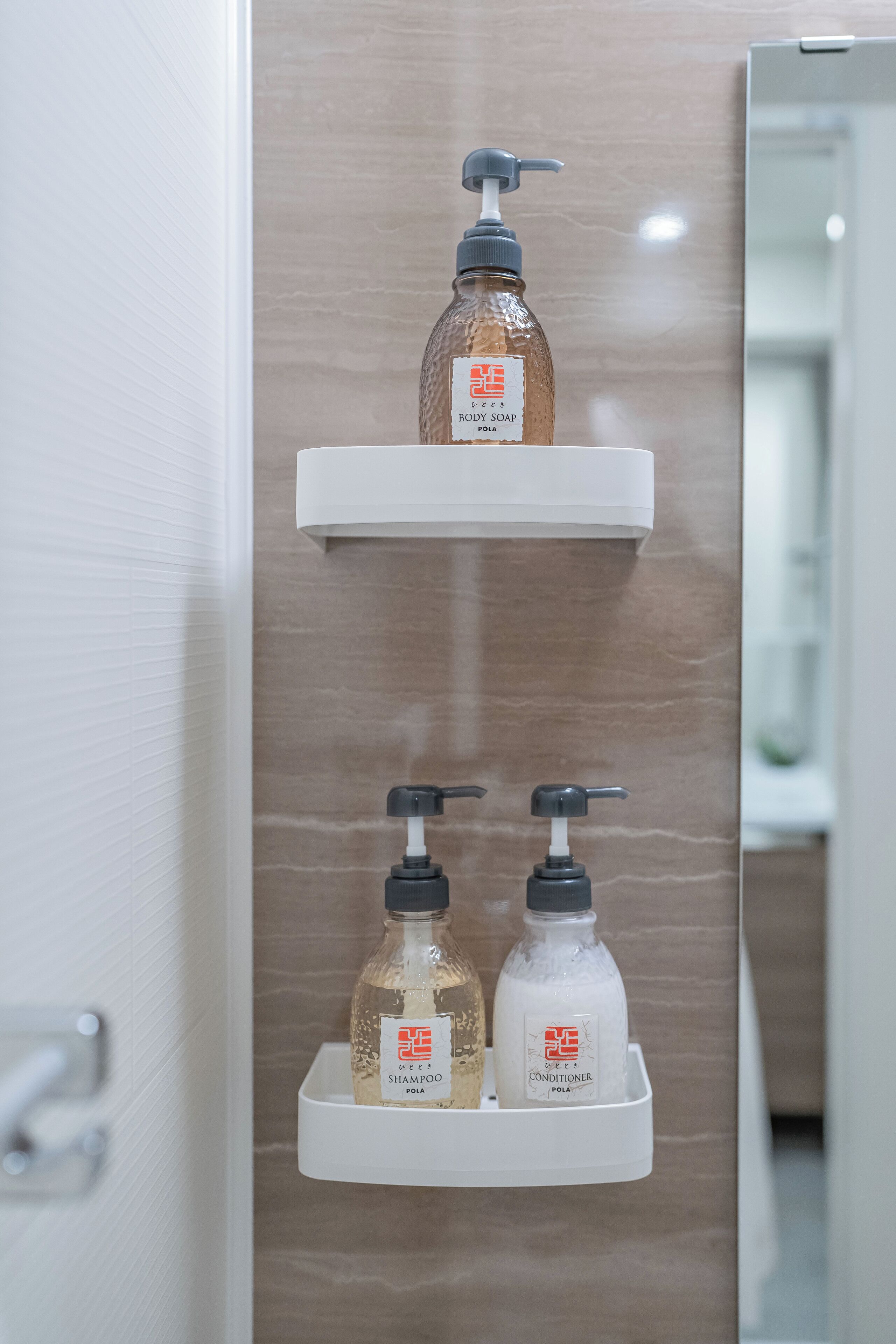 A bathroom with two white shelves holding bottles of shampoo and conditioner.