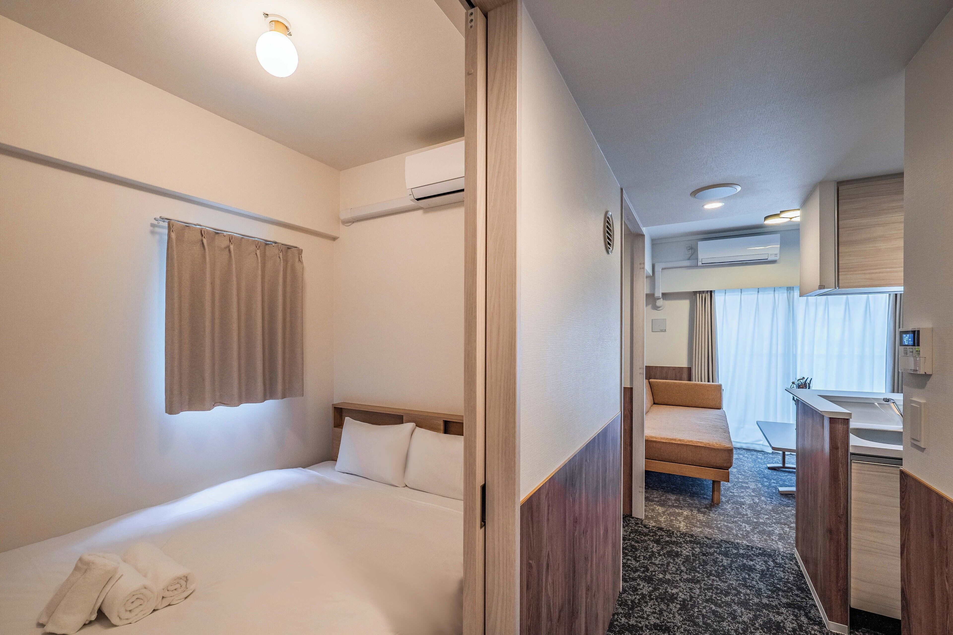 Une chambre d’hôtel comprenant un lit, un petit bureau, une chaise, une salle de bain avec un lavabo et un appareil de climatisation.