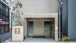 A modern building entrance with a glass door, a small tree, and a sign indicating an apartment hotel. - Apartment Hotel 11 Higashi Umeda (Osaka)