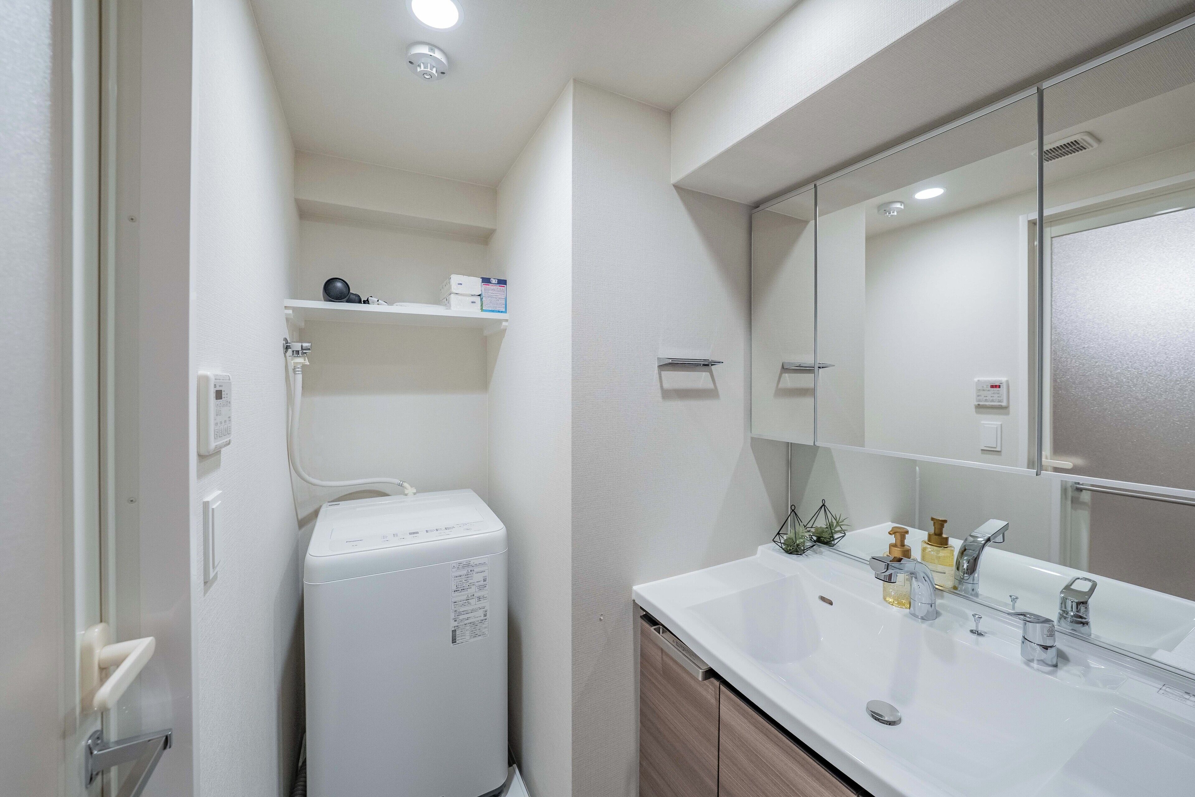 A modern bathroom with a white sink, mirror, and a compact washing machine.