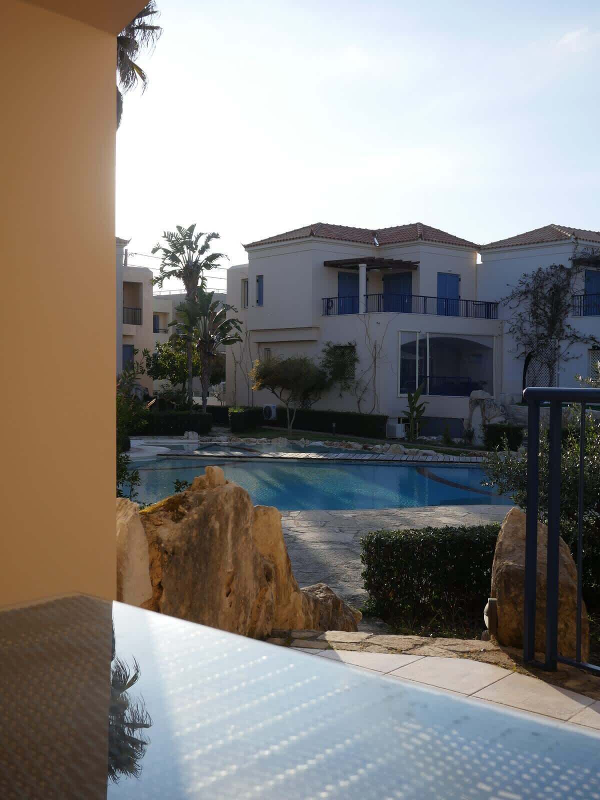 A pool area with a clear view of a building with balconies and a tiled roof.