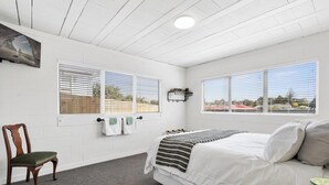 A bedroom with a bed, a chair, and a TV mounted on the wall. - The Bunkers "Urban meets Rustic" (Te Awamutu)