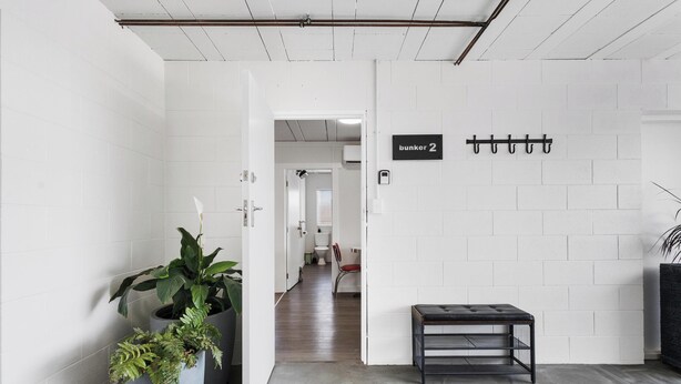 A hallway with white brick walls, a potted plant, a bench, and a sign indicating 'bunker 2'. - The Bunkers "Urban meets Rustic" (Te Awamutu)