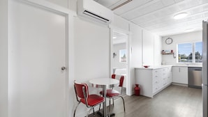 A modern kitchen with white cabinetry, a round dining table with red chairs, and a built-in dishwasher. - The Bunkers "Urban meets Rustic" (Te Awamutu)