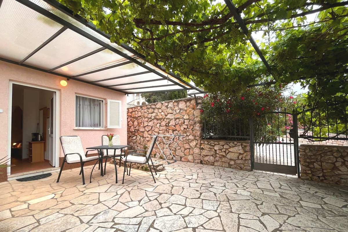 A covered patio with stone flooring, a table with chairs, and a stone wall.