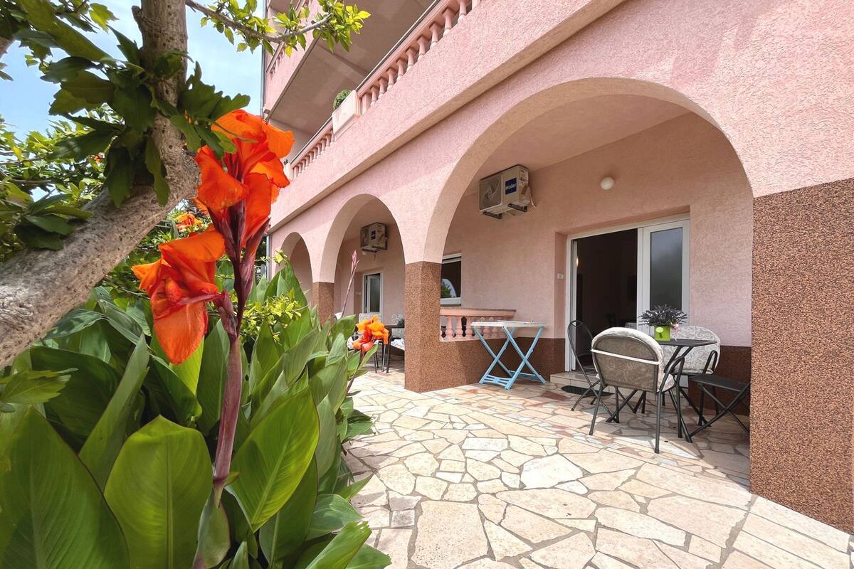A building with a pink facade, stone flooring, and outdoor seating area with tables and chairs.